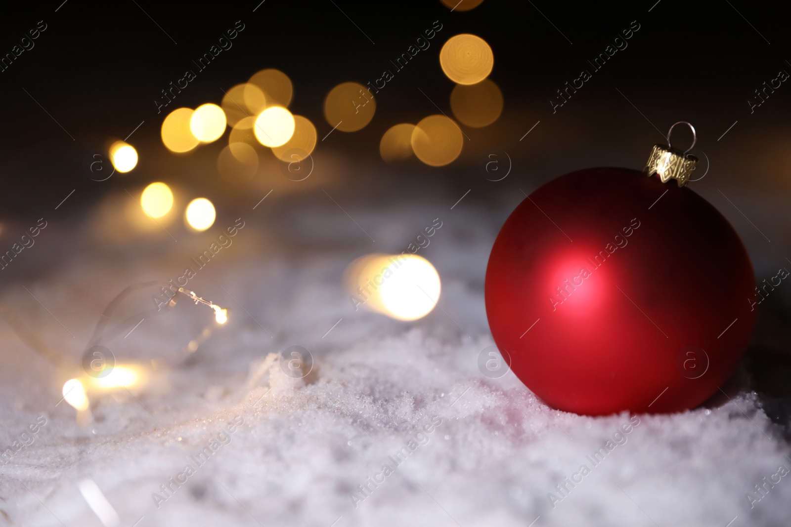 Photo of Christmas ball and fairy lights on white snow outdoors. Space for text