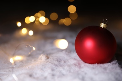 Photo of Christmas ball and fairy lights on white snow outdoors. Space for text