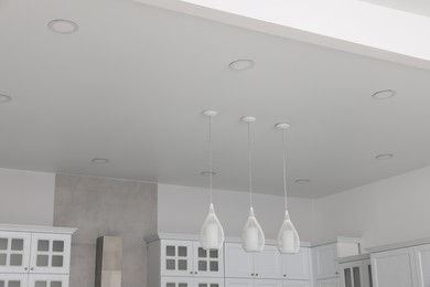 Ceiling with modern lamps, cooker hood and furniture in stylish kitchen