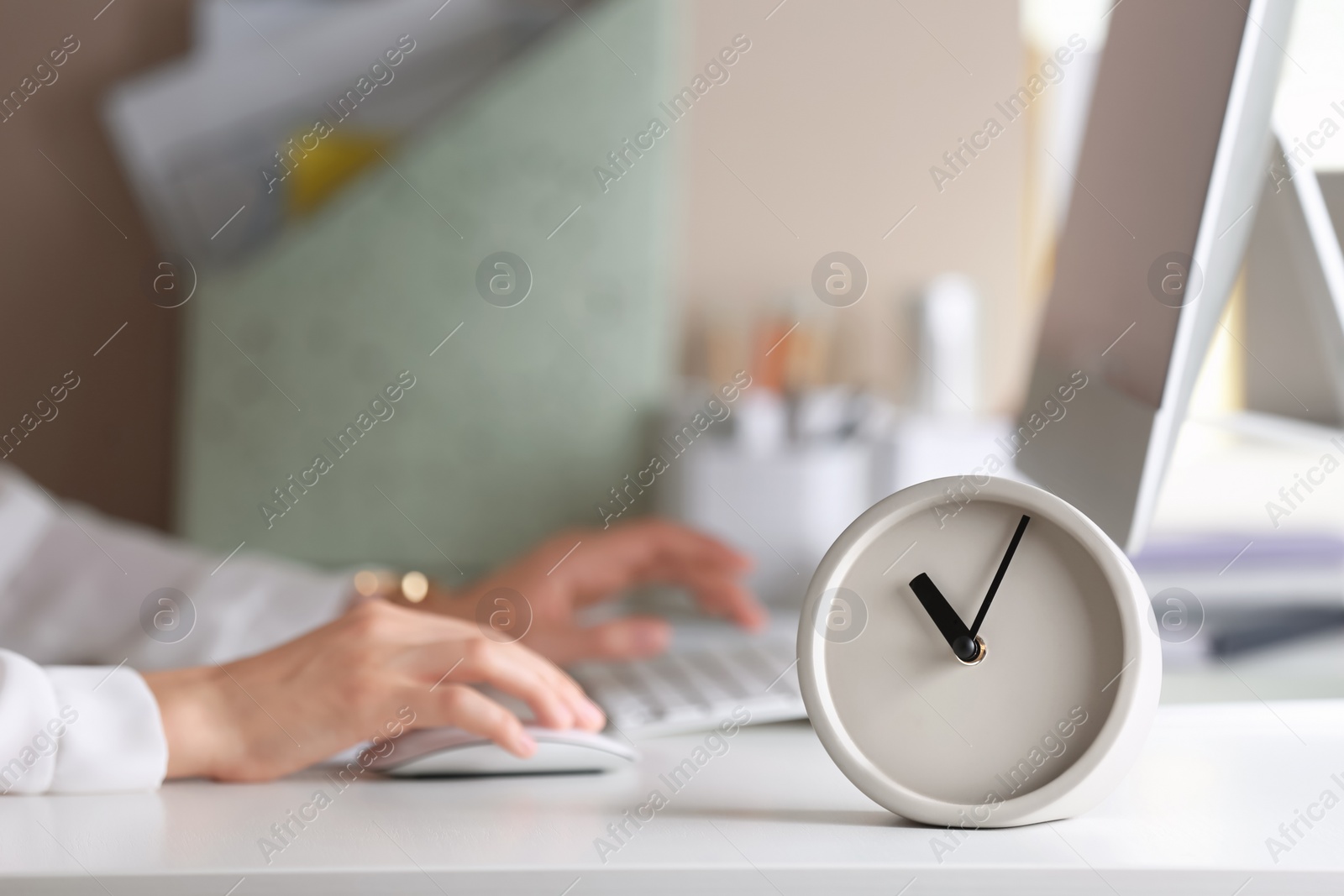 Photo of Alarm clock and blurred woman working on background. Time management