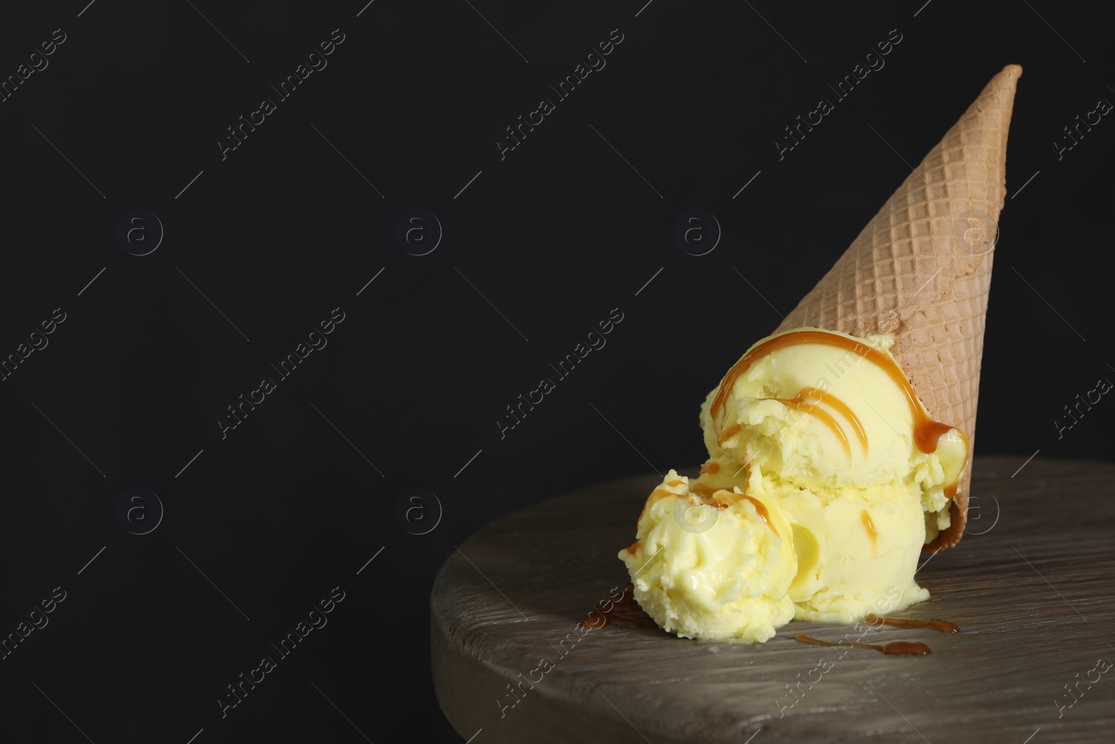 Photo of Delicious yellow ice cream with syrup in wafer cone on table. Space for text