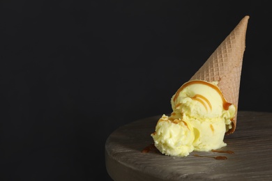 Photo of Delicious yellow ice cream with syrup in wafer cone on table. Space for text