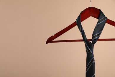 Photo of Hanger with black striped tie on light brown background, closeup. Space for text