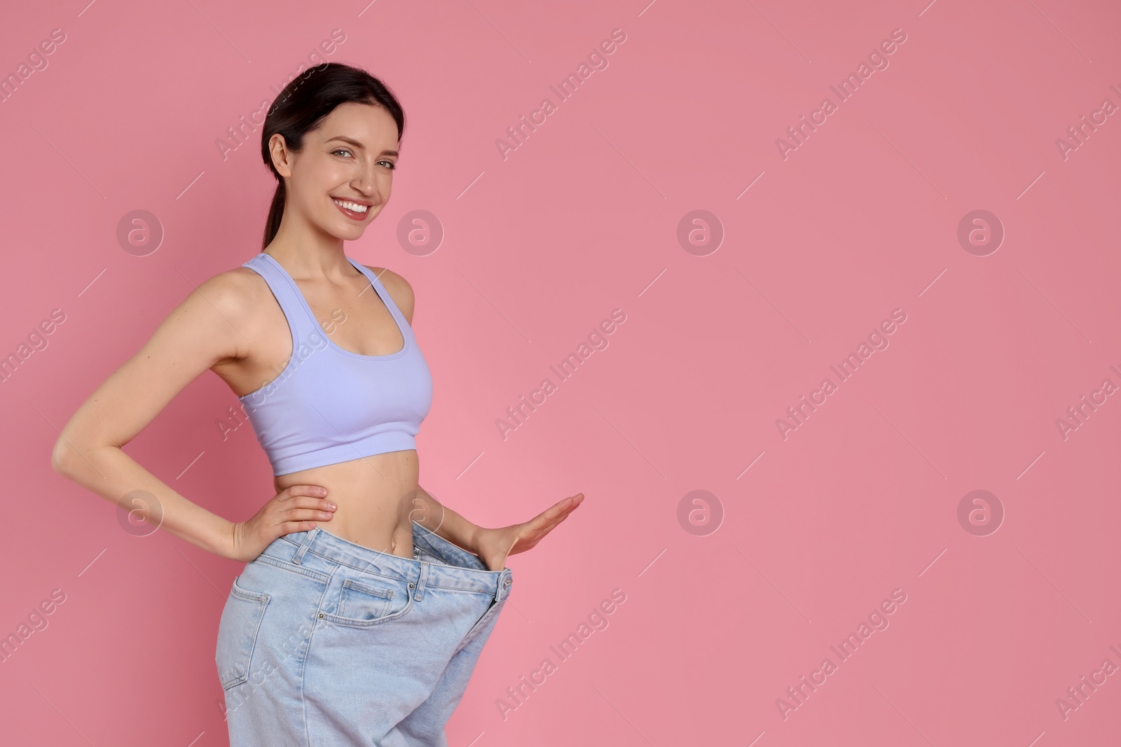 Photo of Happy young woman in big jeans showing her slim body on pink background, space for text