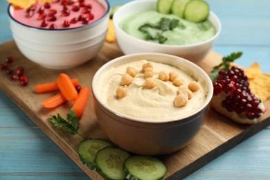 Bowl of delicious classic hummus with vegetables on light blue wooden table