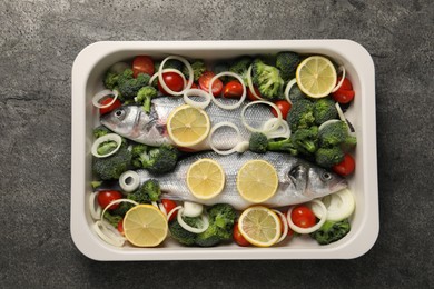 Photo of Raw fish with vegetables and lemon in baking dish on grey textured table, top view