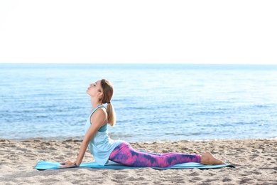 Photo of Young woman doing yoga exercises on beach in morning