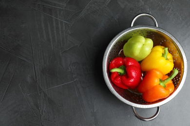 Photo of Colander with wet ripe bell peppers on grey table, top view. Space for text