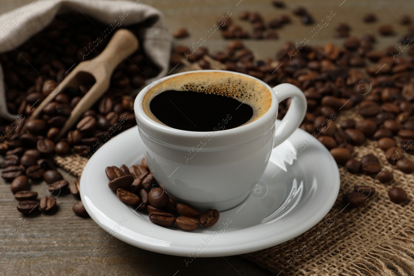 Photo of Cup of aromatic hot coffee and beans on wooden table