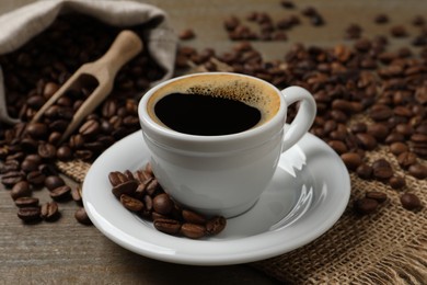 Photo of Cup of aromatic hot coffee and beans on wooden table