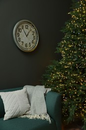 Photo of Beautiful Christmas tree with golden lights, couch and clock on wall in living room