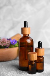 Photo of Glass bottles of essential oil and mortar with different wildflowers on light grey table