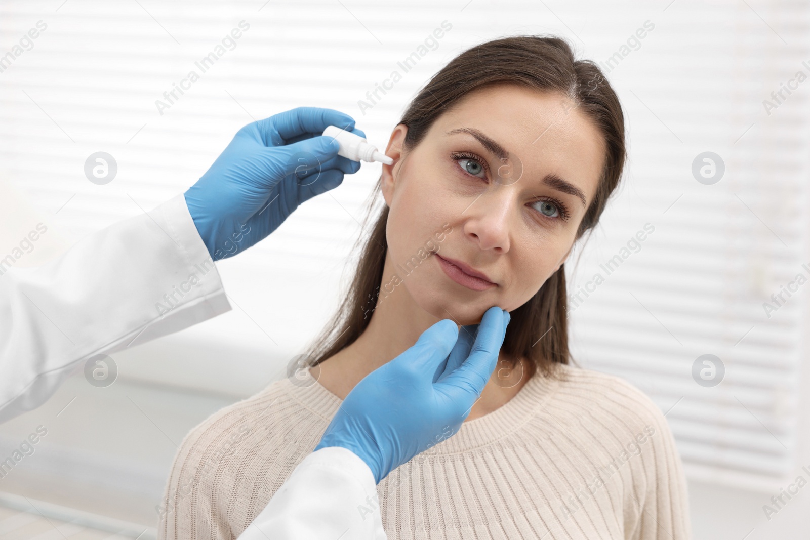 Photo of Doctor applying medical drops into woman's ear indoors