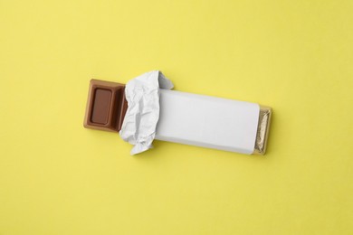 Tasty chocolate bar in package on light yellow background, top view