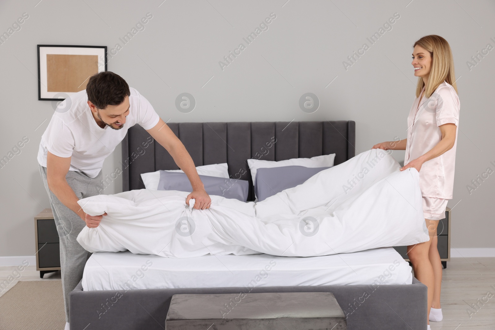 Photo of Couple changing bed linens in room. Domestic chores