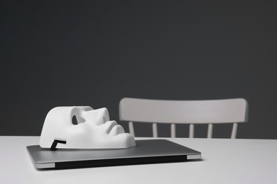 Photo of Mask and laptop on white table against grey background, space for text
