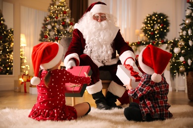 Photo of Santa Claus giving presents to little children in room decorated for Christmas