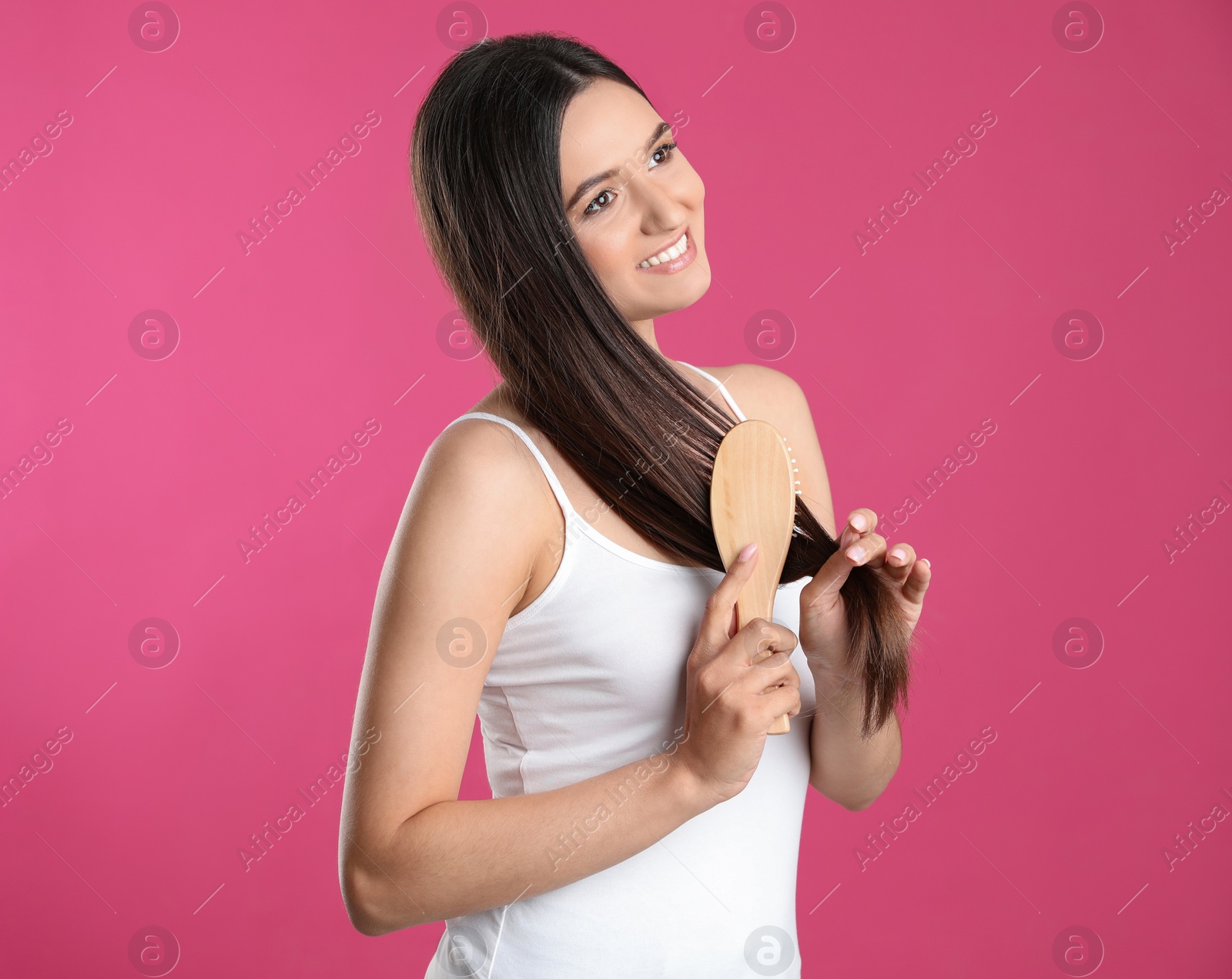 Photo of Beautiful smiling young woman with hair brush on color background