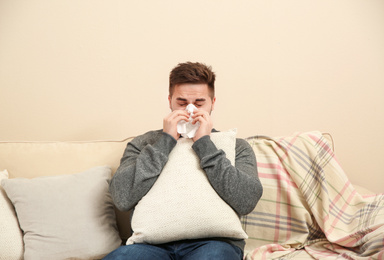 Photo of Sick young man sneezing at home. Influenza virus