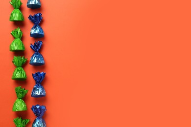 Photo of Many candies in colorful wrappers on orange background, flat lay. Space for text