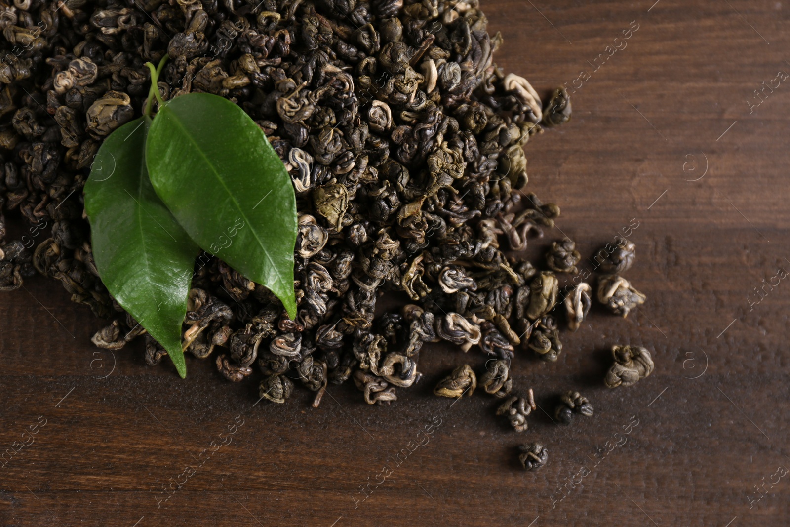 Photo of Heap of dried green tea leaves on wooden table, closeup