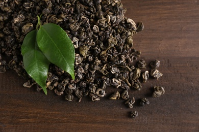 Photo of Heap of dried green tea leaves on wooden table, closeup