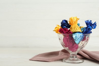 Photo of Candies in colorful wrappers on white wooden table, space for text