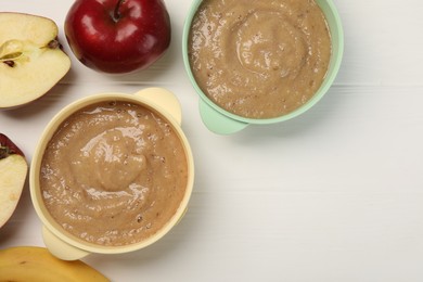 Photo of Bowls with puree and fruits on white wooden table, flat lay and space for text. Baby food