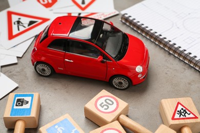 Many different road signs, notebook and toy car on grey table, closeup. Driving school