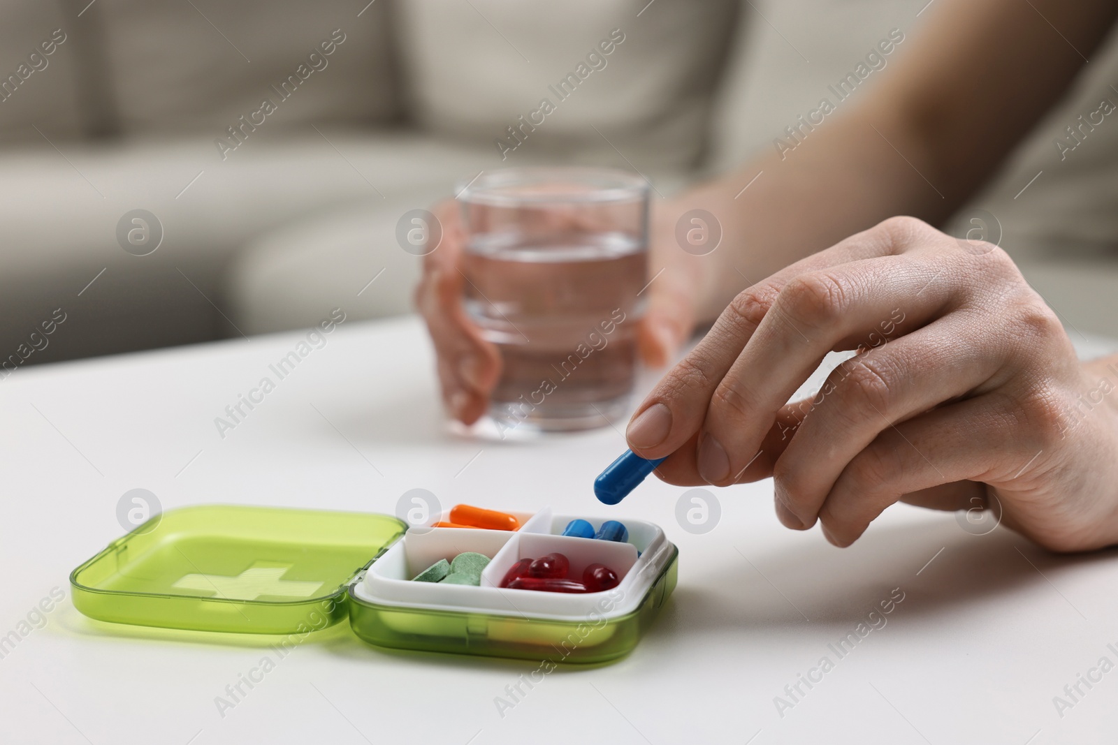 Photo of Woman with pills, organizer and glass of water at white table, closeup