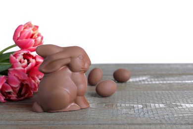 Photo of Chocolate Easter bunny and tulips on grey wooden table against white background. Space for text