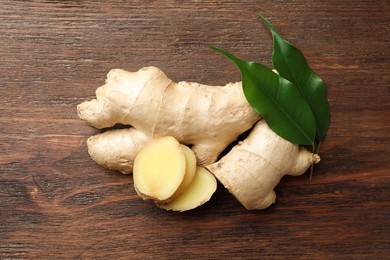 Photo of Cut and whole fresh ginger with leaves on wooden table, top view