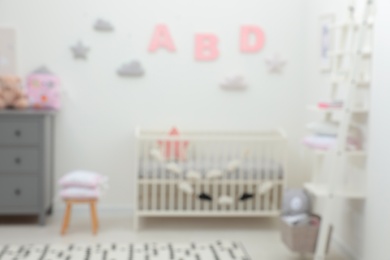 Photo of Blurred view of cute baby room interior with modern crib near white wall