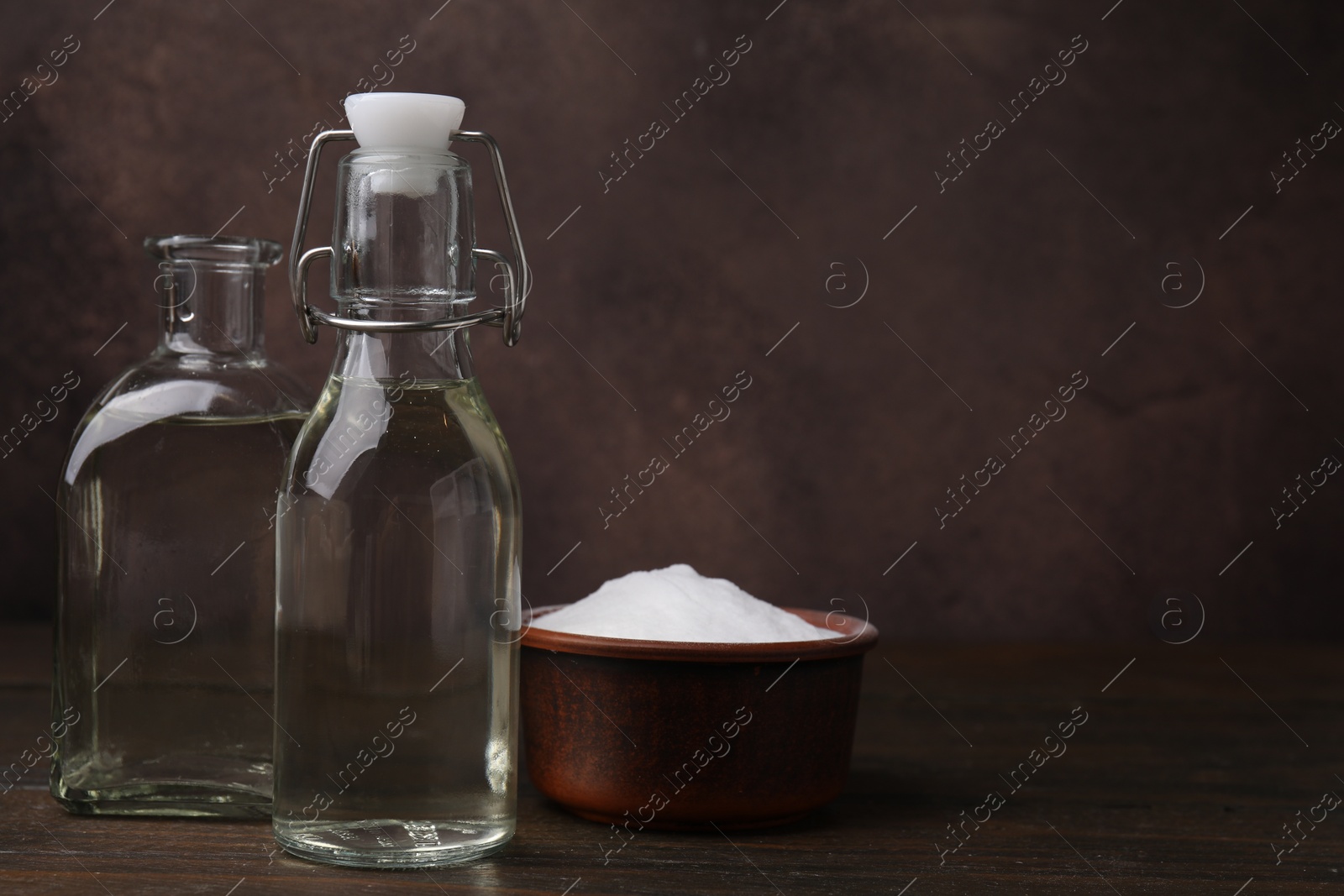 Photo of Vinegar in glass bottles and baking soda on wooden table, space for text