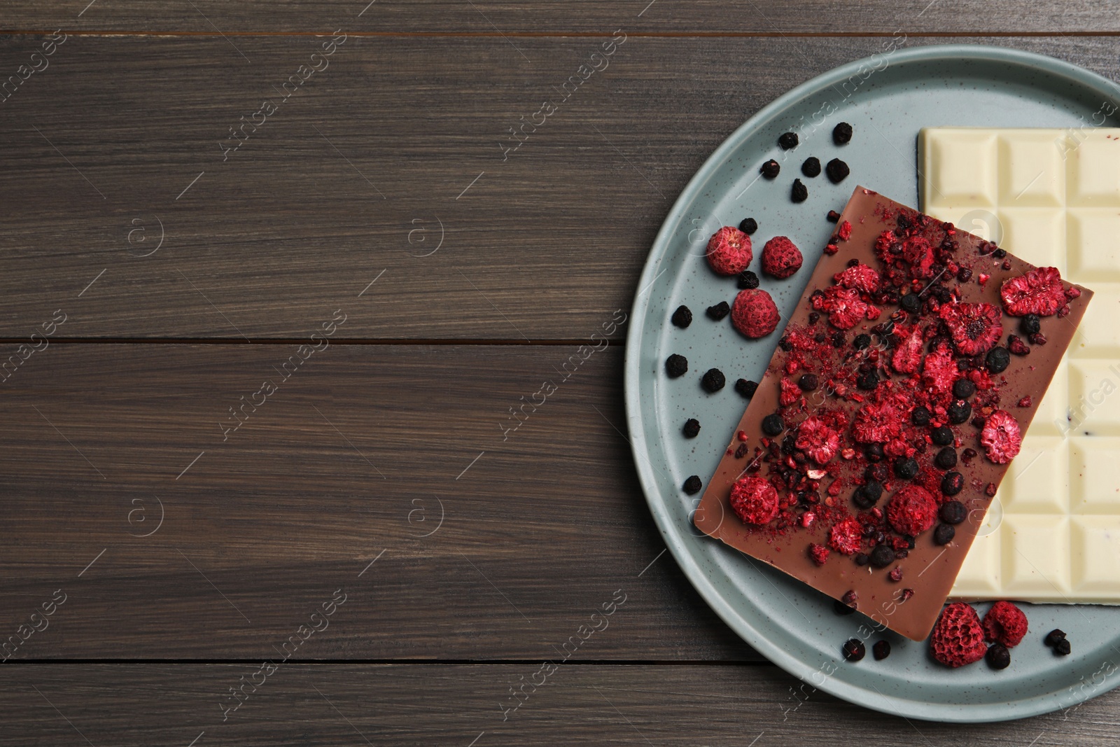 Photo of Plate and different chocolate bars with freeze dried fruits on wooden table, top view. Space for text