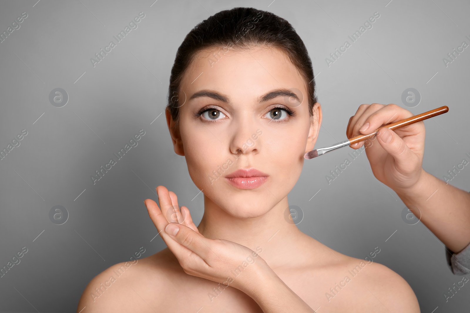 Photo of Visage artist applying makeup on woman's face against grey background. Professional cosmetic products