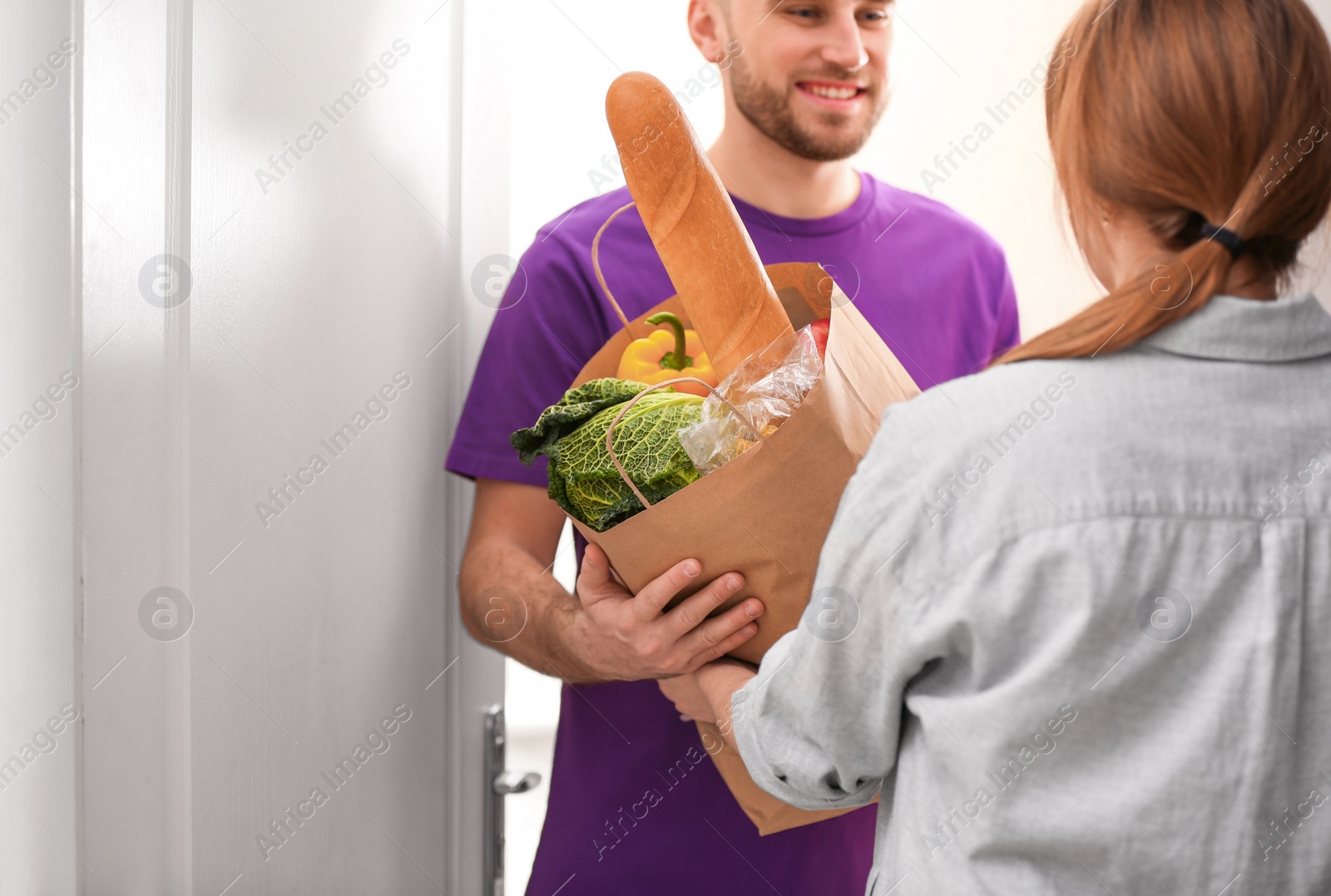 Photo of Courier giving paper bag with products to customer at home, closeup. Food delivery service