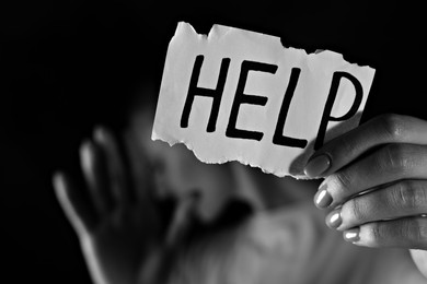 Woman holding piece of paper with word Help on black background, closeup. Domestic violence concept