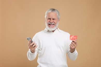 Photo of Upset senior man with credit card and smartphone on beige background. Be careful - fraud