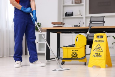 Photo of Cleaning service worker washing floor with mop, closeup. Bucket with wet floor sign in office