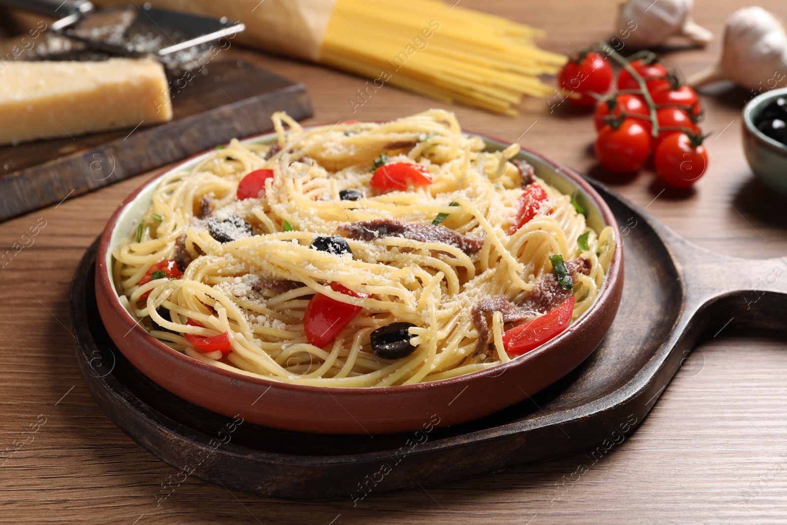 Photo of Plate of delicious pasta with anchovies and ingredients on wooden table