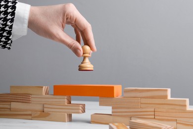 Photo of Businesswoman putting white pawn on bridge made of wooden blocks at table, closeup. Connection, relationships and deal concept