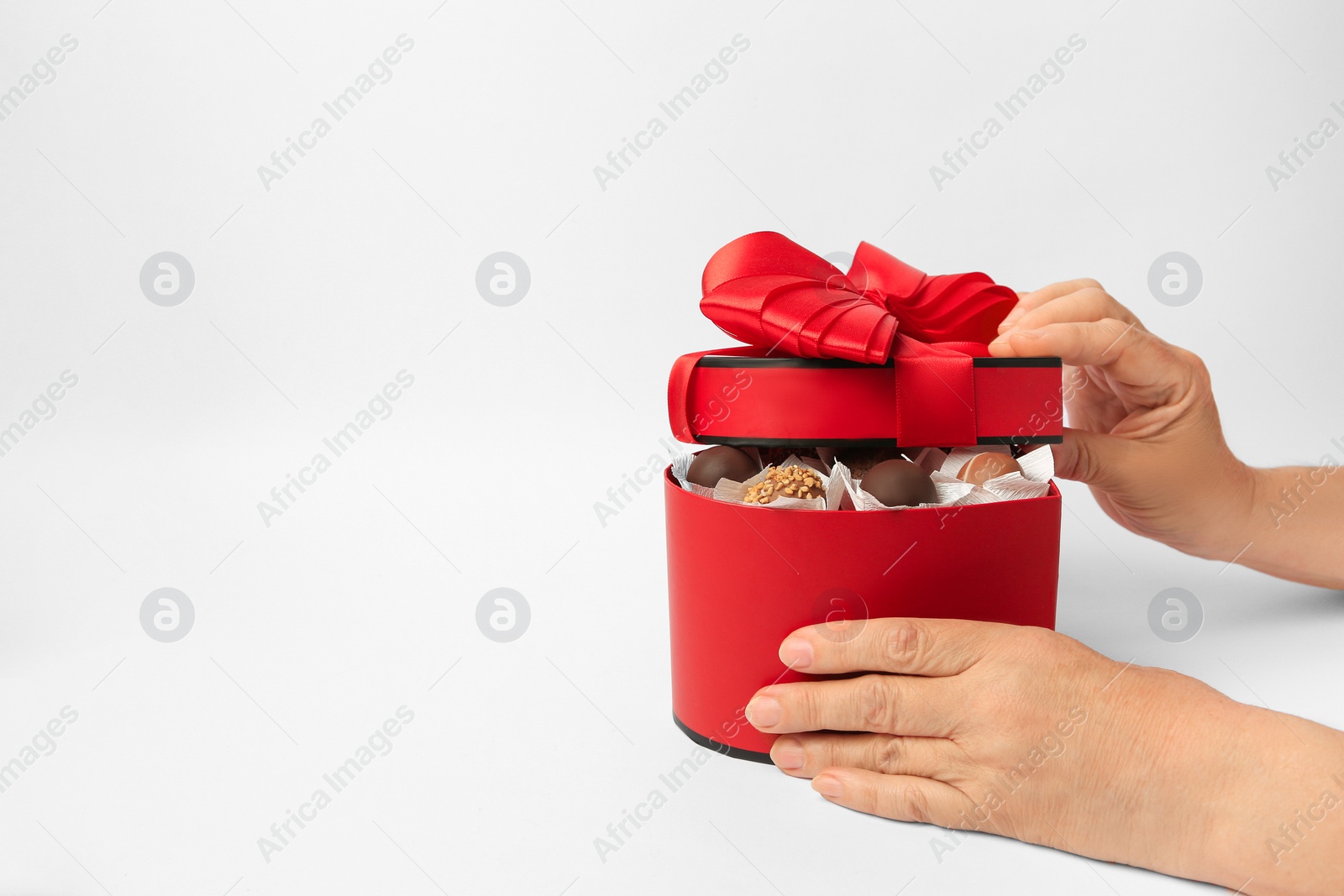 Photo of Woman with box of delicious chocolate candies on white background, closeup. Space for text