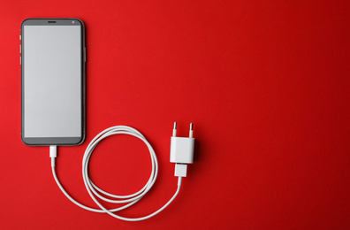 Smartphone and USB charger on red background, flat lay. Space for text