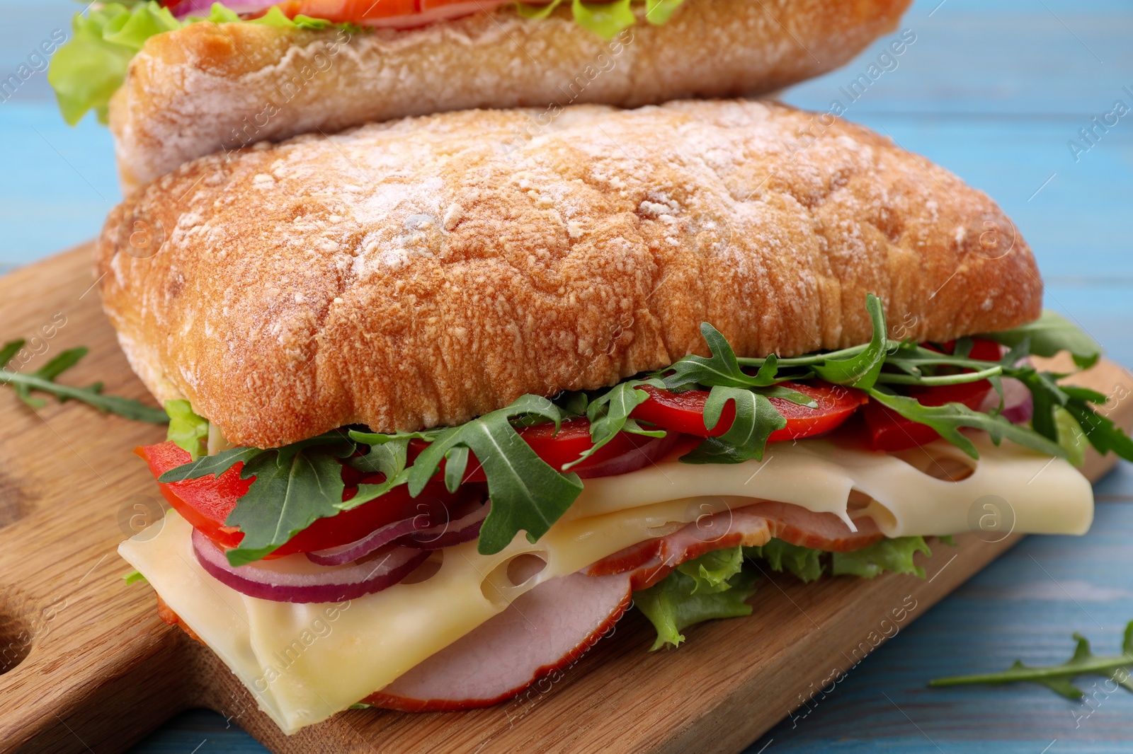 Photo of Delicious sandwich with fresh vegetables, cheese and arugula on wooden board, closeup