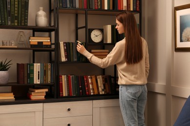 Young woman choosing book on shelf in home library