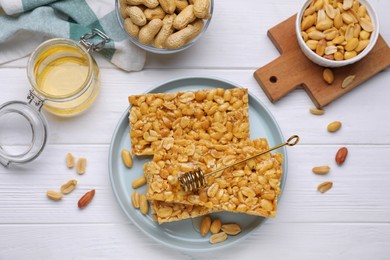 Photo of Delicious peanut bars (kozinaki) and ingredients on white wooden table, flat lay