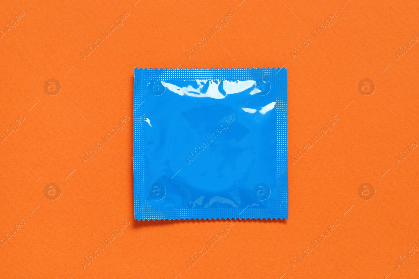 Photo of Condom package on orange background, top view. Safe sex