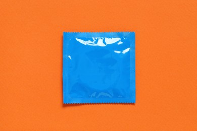 Photo of Condom package on orange background, top view. Safe sex