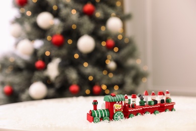 Photo of Bright toy train on artificial snow in room with Christmas tree